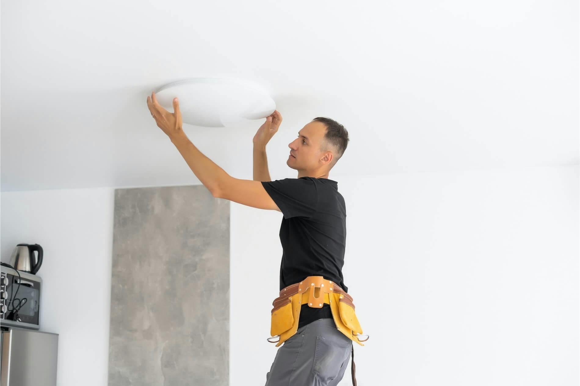Electrician installs overhead lighting cover in kitchen