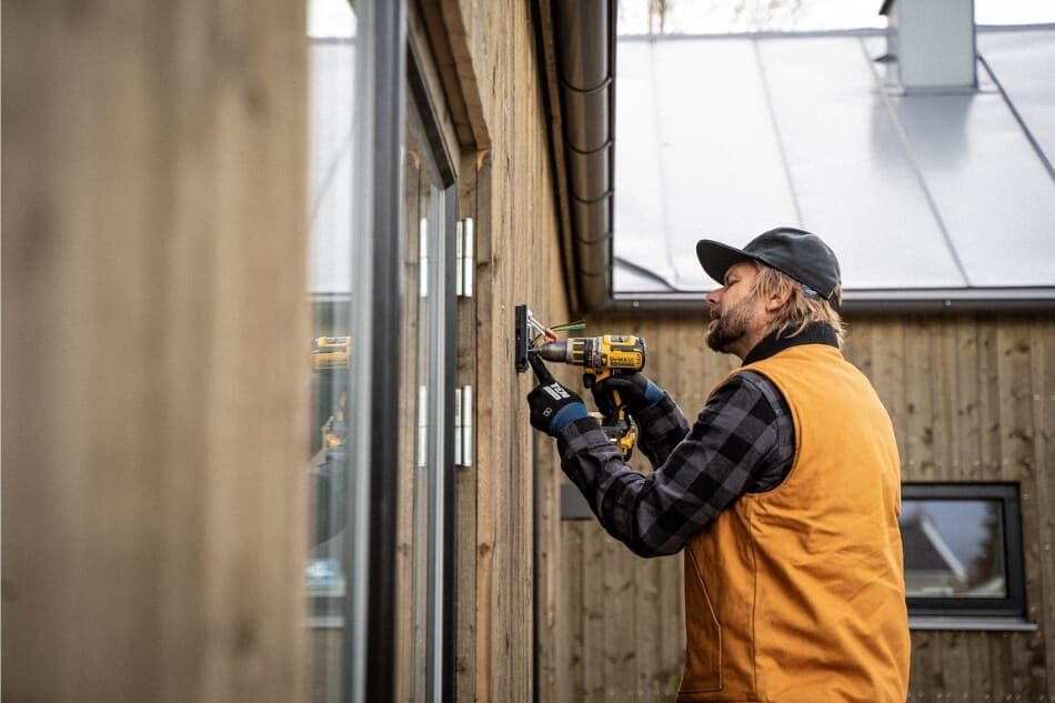 Electrician with Dewalt power drill fastens an outdoor electrical outlet to wall